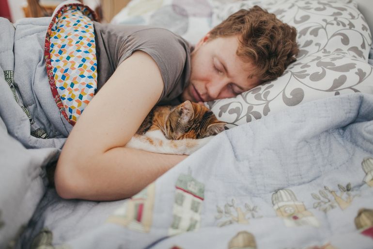 young man lying in the bed with the tabby cat sleeping