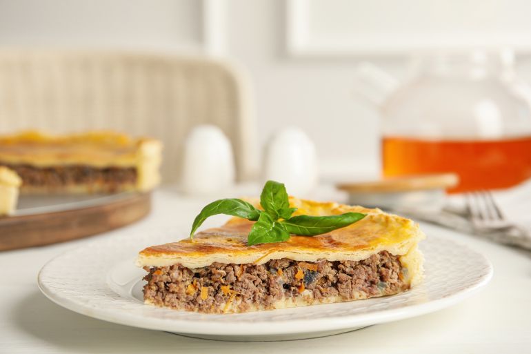 Piece of delicious pie with minced meat on white table indoors