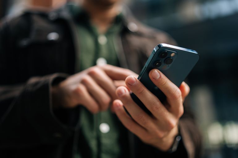 5ytdf-1770115661 Close-up hands of unrecognizable man holding and using smartphone standing on city street, browsing internet, checking social media, using mobile application. Concept of modern communication.