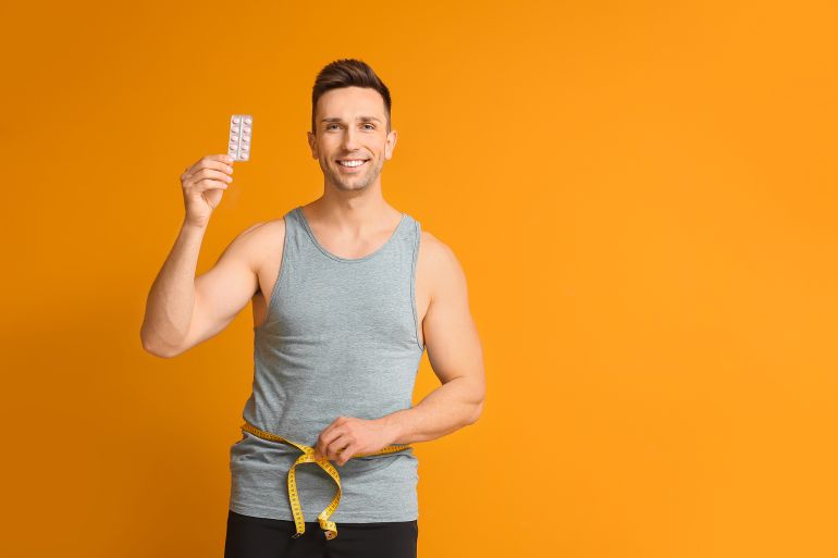 Young man with weight loss pills and measuring tape on color background