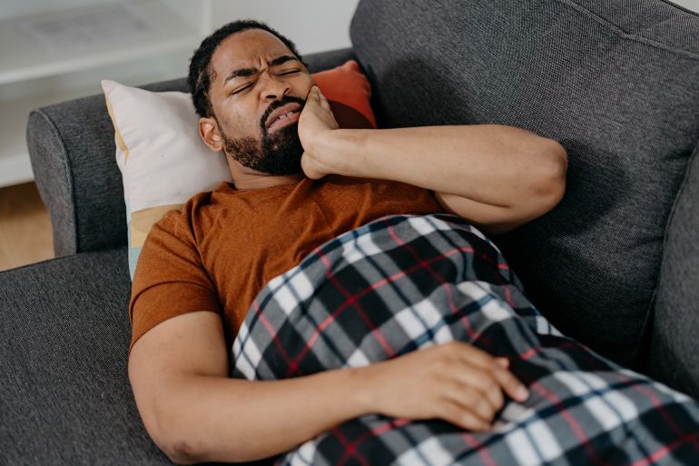 A young African American man is lying on a sofa, having a bad toothache.