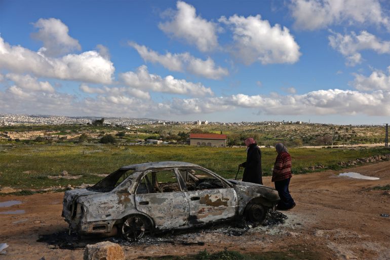 afp_69a05ae23aea-1772116706 Palestinians walk past a burnt car after it was reportedly set on fire by Israeli settlers from a nearby settlement, in Susya village, south of Hebron in the Israeli-occupied West Bank, on February 25, 2026.