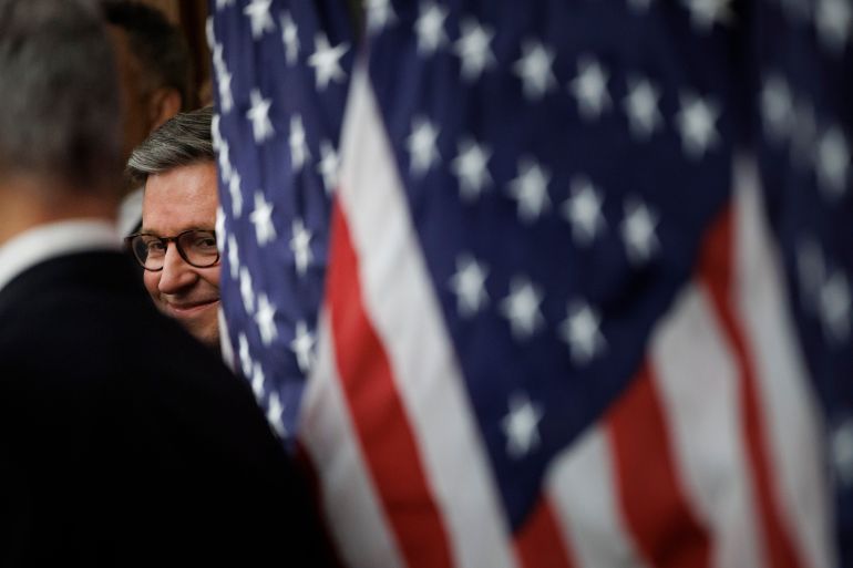 House Speaker Mike Johnson, R-La., peers through American flags during a news conference on the SAVE America Act on Capitol Hill in Washington, Wednesday, Feb. 11, 2026, in Washington. (AP Photo/Tom Brenner)