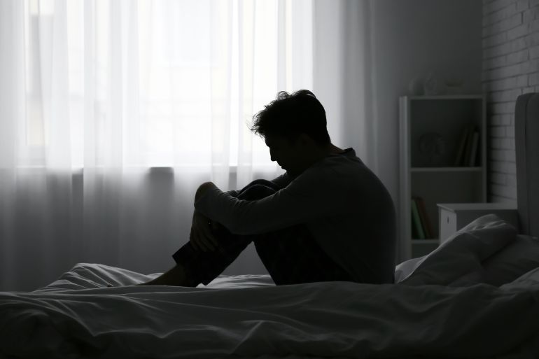Silhouette of depressed young man sitting in dark bedroom