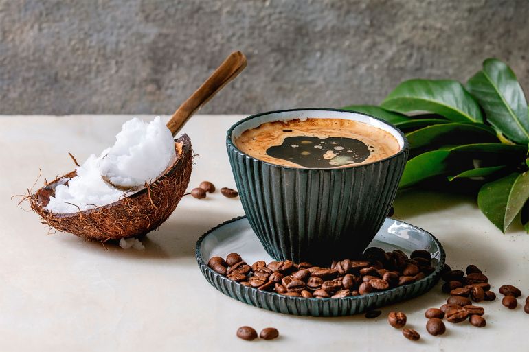 Bulletproof coffee. Keto diet coffee in blue ceramic cup with organic coconut cold press oil in spoons with beans and green branch on white marble table. Grey wall at background. Bulletproof coffee. Keto diet coffee in blue ceramic cup with organic coconut cold press oil in spoons with beans and green branch on white marble table. Grey wall at background. (Photo by: Natasha Breen/REDA&CO/Universal Images Group via Getty Images)