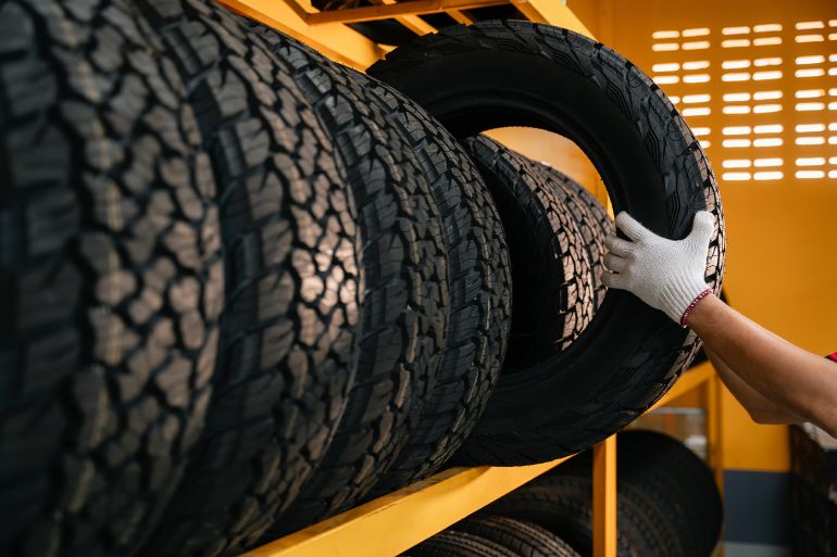 gettyimages-1326100517-1758639062-1 hand of a tire changer lifting a car tires out of a warehouse.