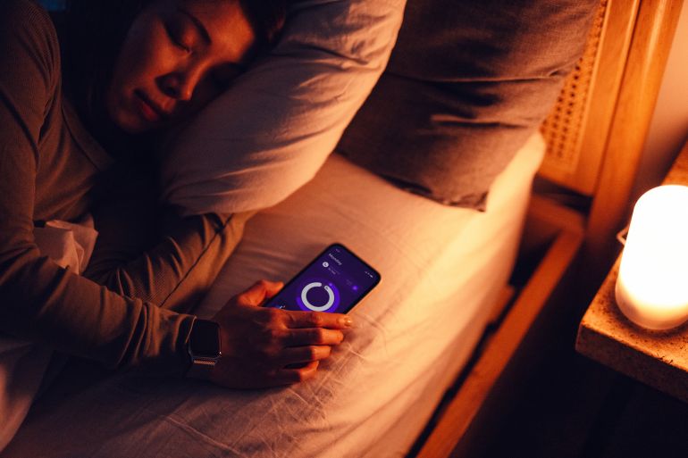Young woman using healthcare app on smartphone to improve sleep while lying in bed. Healthcare and technology.