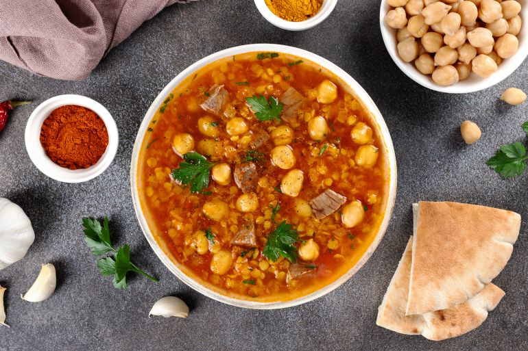 Moroccan harira soup with ingredients, spices and arabic bread on grey background. Top view. Ramadan iftar food.