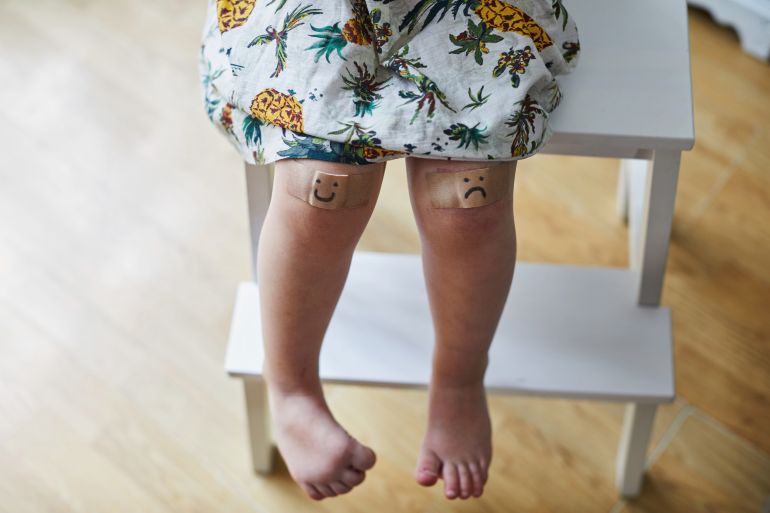 اللصقات الطبية Toddler girl with two plasters on her grazed knees one with a sad face and one with a smiley face drawn on