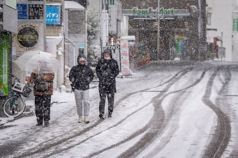 People walk down a street during a snowfall in Tokyo on February 8, 2026. (Photo by Yuichi YAMAZAKI / AFP)