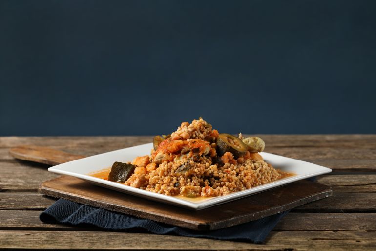 Maftoul – Palestinian Couscous with chicken and tomato sauce in white dish on wood table ; Shutterstock ID 2074149389; purchase_order: aj; job: ; client: ; other: