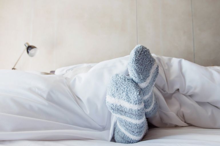 Female foot in warm Stripe wool sock ,Relaxing in bed concept