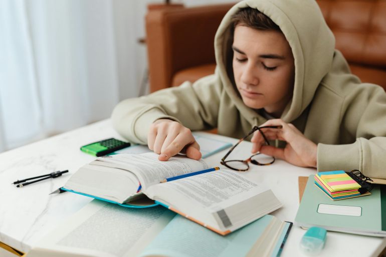 Young Man In Beige Hoodie Reading And Studying At Home