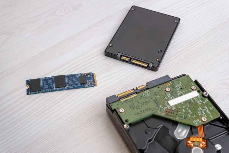 M2 SSD drive placed near SATA SSD and opened hard disk drive on light wooden desk, computer storage components comparison