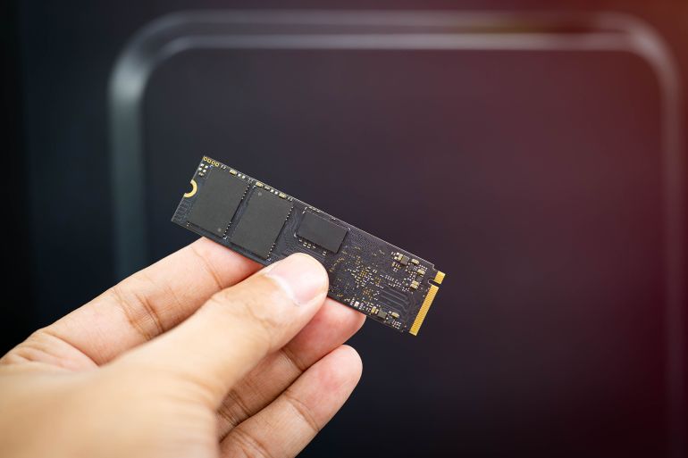 Close-up of a hand holding an NVMe M.2 SSD, a high-speed solid-state drive for modern laptops and PCs, isolated on dark background with copy space, ideal for tech or IT concepts.