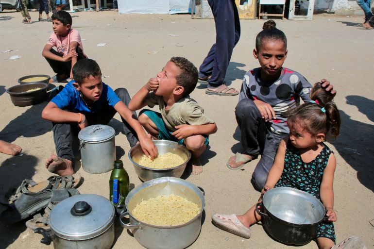 afp_68af1d7badbb-1756306811 TOPSHOT - Palestinian children eat cooked rice after managing to get portions of hot food from a charity kitchen in Khan Yunis in the southern Gaza Strip on August 27, 2025.