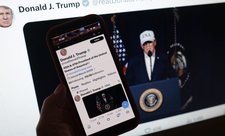 afp_69a2ed205a1e-1772285216 This illustration image shows a person looking at a smartphone displaying US President Donald Trump making a statement regarding combat operations on Iran, alongside a computer screen featuring the same message posted on X on February 28, 2026.