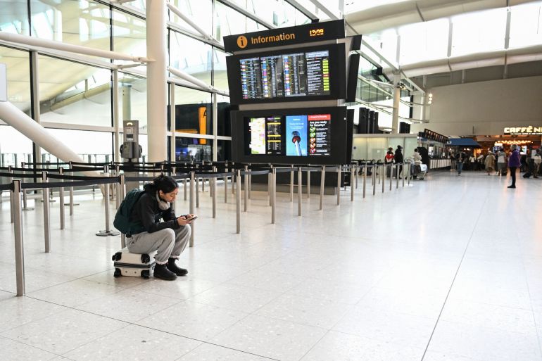 A passenger sits on her suitcase in an empty section of the check-in area at London Heathrow Airport in west London on March 1, 2026, as flights are severely disrupted following the US and Israel's strikes on Iran.