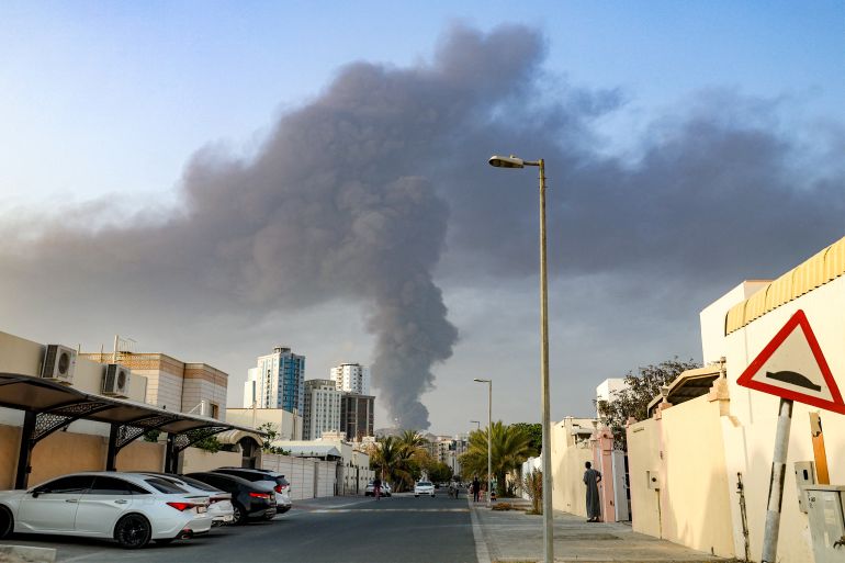 TOPSHOT - People watch from a street as a tall smoke plume billows following an explosion in the Fujairah industrial zone on March 3, 2026.