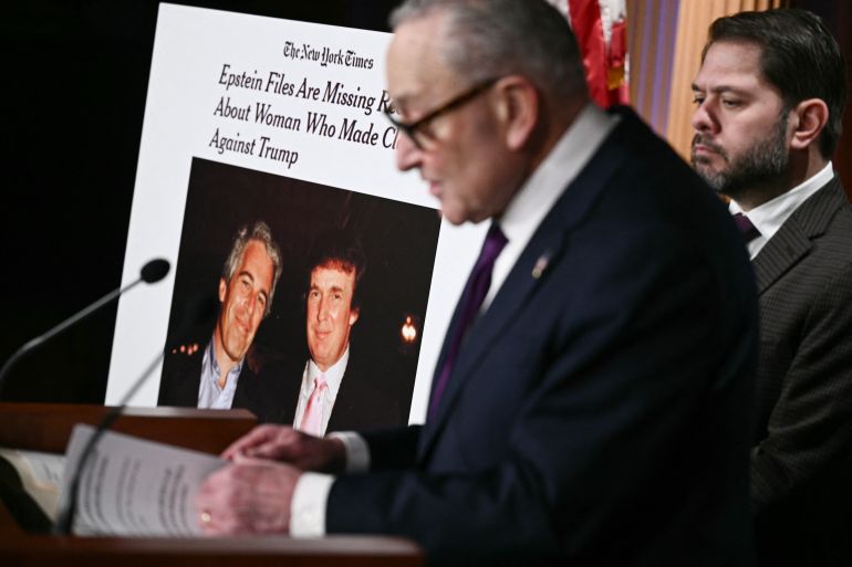 A sign showing a photo of US President Donald Trump and Jeffrey Epstein is displayed as US Senate Minority Leader Chuck Schumer, Democrat of New York, and US Senator Ruben Gallego, Democrat from Arizona speak during a conference to announce oversight efforts on the files of convicted sex offender Jeffrey Epstein, at the US Capitol in Washington, DC, on February 26, 2026. (Photo by Brendan SMIALOWSKI / AFP)