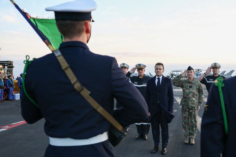 French President Emmanuel Macron (C) reviews troops as he visits the French aircraft carrier Charles de Gaulle, deployed to the Mediterranean following Iranian drone strikes on Cyprus on the Mediterranean Sea, on March 9, 2026, on the sidelines of his trip to Cyprus to discuss regional security. (Photo by Gonzalo Fuentes / POOL / AFP)