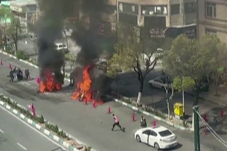 TOPSHOT - This video grab taken from UGC images posted on social media on March 17, 2026, appears to show a motorcycle ablaze following a strike on a Basij checkpoint in Tehran, as people pull a person away from the fire.