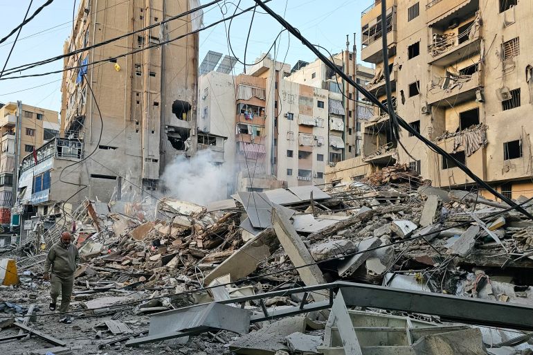 TOPSHOT - A man walks past debris at the site of an overnight Israeli airstrike in Beirut's southern suburb of Bir al Abed on March 24, 2026.