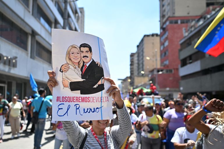 afp_69c4c172a247-1774502258 A woman holds up a poster depicting Venezuelan deposed President Nicolas Maduro and his wife, Cilia Flores, during a march demanding the complete lifting of US sanctions in Caracas on March 23, 2026. (Photo by Juan BARRETO / AFP)