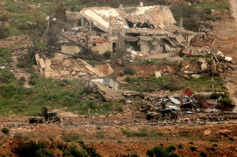 afp_69c59b964873-1774558102 Israeli military vehicles move past destroyed buildings in southern Lebanon close to the Israeli border on March 26, 2026.