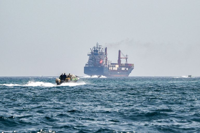 (FILES) A boat approaches the St Kitt's and Nevis-flagged container ship Marsa Victory while crusing in the waters of the Strait of Hormuz off the coast of Khasab in Oman’s northern Musandam peninsula on June 25, 2025.