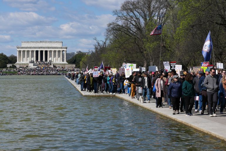 afp_69c8105e03af-1774719070 Demonstrators march along the reflecting pool near the Lincoln Memorial during the "No Kings" national day of protest in Washington, DC, on March 28, 2026.