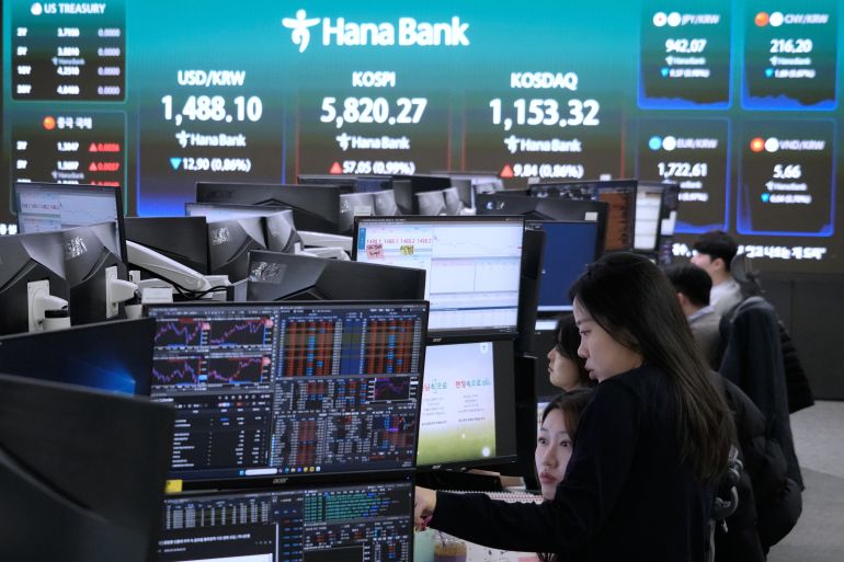 Currency traders watch monitors near a screen showing the Korea Composite Stock Price Index (KOSPI), top center, and the foreign exchange rate between U.S. dollar and South Korean won, top center left, at the foreign exchange dealing room of the Hana Bank headquarters in Seoul, South Korea, Friday, March 20, 2026. (AP Photo/Ahn Young-joon)