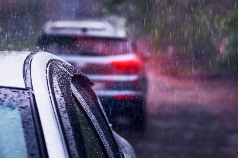Heavy rain falls on the roof of a car during a thunderstorm. Red brake light in the dark. The concept of auto insurance and natural disasters. Driving on cloudy rainy days. Selective focus.