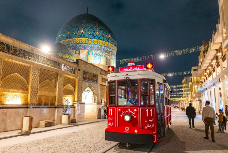 مشهد ليلي لترام الرشيد تحيط به أضواء المحال والمساجد في أحد أقدم شوارع بغداد.