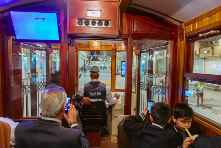 العربة الحمراء تتوقّف لتحميل ركّاب جدد، بينما تظل عدسات الهواتف مرفوعة توثّق اللحظة