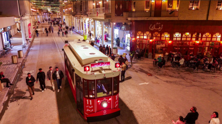 باعة ومقاه على جانبي الشارع يراقبون مرور الترام الذي أعاد الحركة التجارية إلى المنطقة