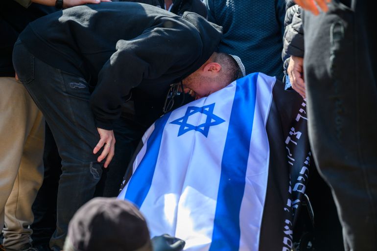 BEIT SHEMESH, ISRAEL - MARCH 02: Itamar Elimelech, son of Sara Elimelech places his head on his mother's body before it is lowered into the ground during the burial for her and her adault daughter Ronit Elimelech, killed in yesterday's Iranian missile strike here on March 2, 2026 in Beit Shemesh, Israel. Ronit and her three children were visiting her mother, Sara, when the sirens went off and the family entered a public shelter, according to a statement from United Hatzalah. Sara's husband and her three grandchildren survived the attack. Iran fired waves of missiles at Israel after the United States and Israel launched a joint attack on Iran early on February 28th. Israel's Defense Minister Israel Katz declared a state of emergency, as Israelis braced for the retaliation. (Photo by Alexi J. Rosenfeld/Getty Images)