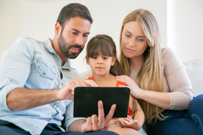 d8b9d8a7d8a6d984d8a9-d8a3d8aed8a8d8a7d8b1-1773837961 Focused young parents and cute daughter sitting on couch, using tablet, staring at screen, watching video together.