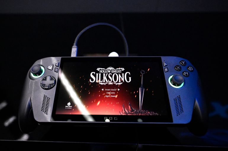A photo shows the new ROG Xbox Ally X from ASUS and Xbox with the Hollow Knight: Silksong video game at the Xbox booth during the Gamescom video games trade fair at the Trade Fair Center in Cologne, western Germany, on the first day of the fair on August 20, 2025. The 2025 edition of the vast Gamescom trade fair in Cologne, Germany, had its opening night on August 19, 2025 and will be running from August 20 to 24, 2025. (Photo by Ina FASSBENDER / AFP)