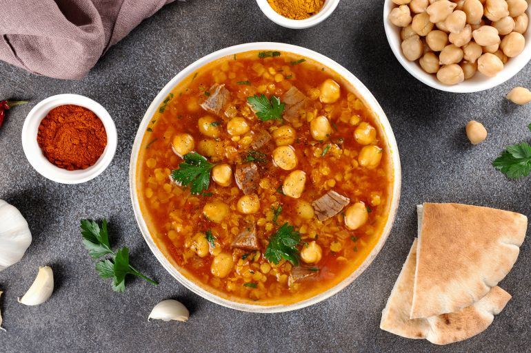 Moroccan harira soup with ingredients, spices and arabic bread on grey background. Top view. Ramadan iftar food.