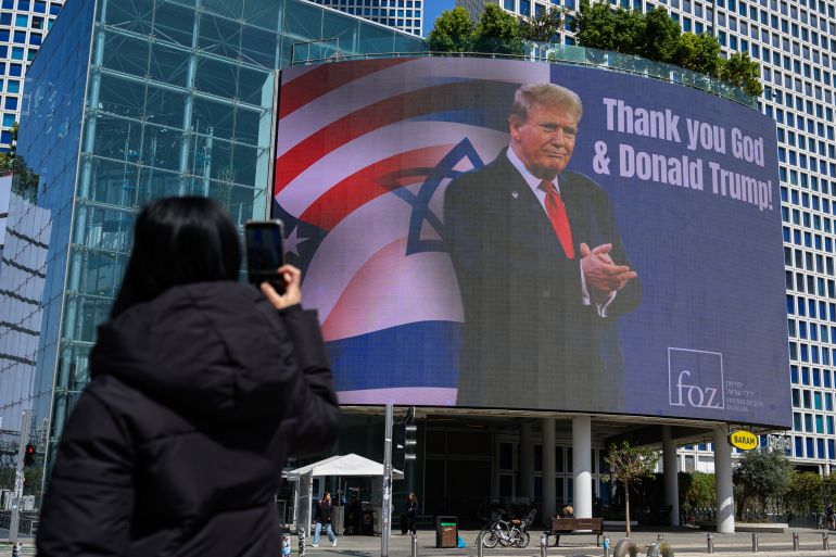 TEL AVIV, ISRAEL - MARCH 12: A person takes a photo of a billboard of U.S. President Donald Trump next to the words, "thank you God & Donald Trump" on March 12, 2026 in Tel Aviv, Israel. Iran has continued firing waves of drones and missiles at Israel after the United States and Israel launched a joint attack on Iran early on February 28th. (Photo by Alexi J. Rosenfeld/Getty Images)