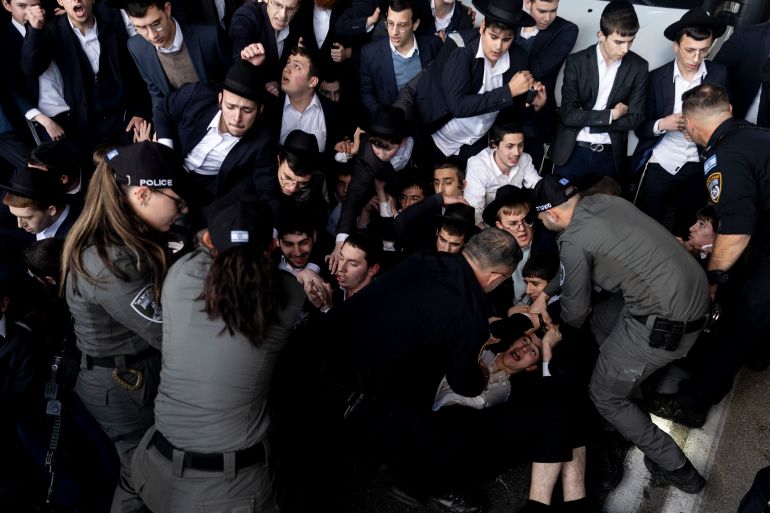 getty_69c42815d7-1774462998 BNEI BRAK, ISRAEL - DECEMBER 28: Ultra-Orthodox Jewish men clash with police officers as they block a main highway during a demonstration against drafting into the Israeli army on December 28, 2025 in Bnei Brak, Israel. Ultra-Orthodox Jewish groups, including the extremist Jerusalem Faction, are protesting the reported arrests of Haredi men who have recently refused conscription to the Israel Defence Forces (IDF). The demonstration is taking place as a draft bill is being considered by lawmakers in Israel's Knesset, which would end the conscription exemption for military aged ultra-Orthodox men, known as Haredi, who are enrolled in yeshivas for full-time religious study. Last year Israel's High Court of Justice ruled that the IDF must begin drafting Haredi men after the exemption law expired in June 2023. The controversial issue has split the nation following Israel's military occupation of Gaza in the wake of the October 7, 2023 Hamas attacks, and threatens the viability of Prime Minister Benjamin Netanyahu's coalition government. (Photo by Amir Levy/Getty Images)