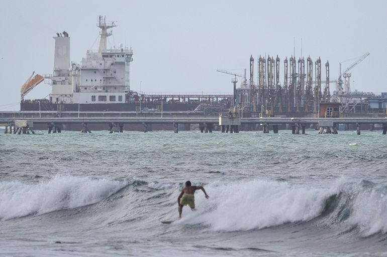 PUERTO CABELLO, VENEZUELA - DECEMBER 18: A man surfs as an oil tanker is seen anchored at the dock in the outskirts of 'El Palito' refinery on December 18, 2025 in Puerto Cabello, Venezuela. President Trump stated on December 17th that Venezuela took away oil rights from the US. Trump's administration has sanctioned Venezuelan oil with blockades, while many US Navy units are deployed off the coast of Venezuela under the premise of combating the drug cartels. (Photo by Jesus Vargas/Getty Images)