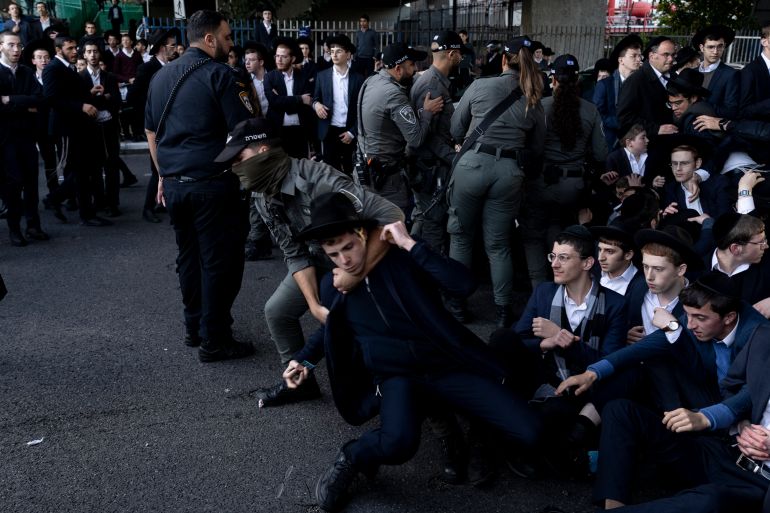 BNEI BRAK, ISRAEL - DECEMBER 28: Ultra-Orthodox Jewish men clash with police officers as they block a main highway during a demonstration against drafting into the Israeli army on December 28, 2025 in Bnei Brak, Israel. Ultra-Orthodox Jewish groups, including the extremist Jerusalem Faction, are protesting the reported arrests of Haredi men who have recently refused conscription to the Israel Defence Forces (IDF). The demonstration is taking place as a draft bill is being considered by lawmakers in Israel's Knesset, which would end the conscription exemption for military aged ultra-Orthodox men, known as Haredi, who are enrolled in yeshivas for full-time religious study. Last year Israel's High Court of Justice ruled that the IDF must begin drafting Haredi men after the exemption law expired in June 2023. The controversial issue has split the nation following Israel's military occupation of Gaza in the wake of the October 7, 2023 Hamas attacks, and threatens the viability of Prime Minister Benjamin Netanyahu's coalition government. (Photo by Amir Levy/Getty Images)