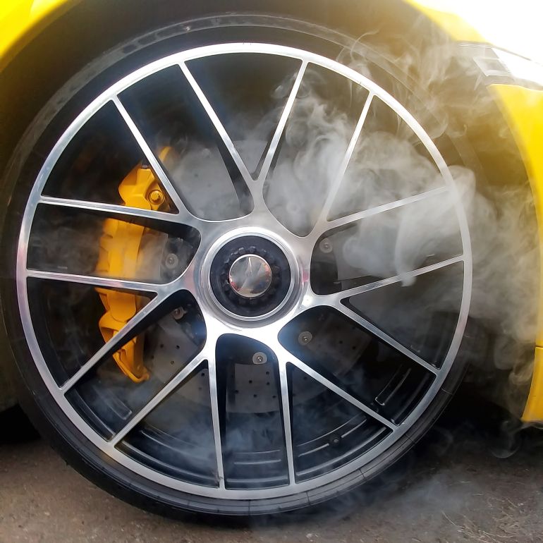 مكابح الكربون-السيراميك Yellow car with light alloy wheels with carbon ceramic brakes and smoke from it. Close up, square image