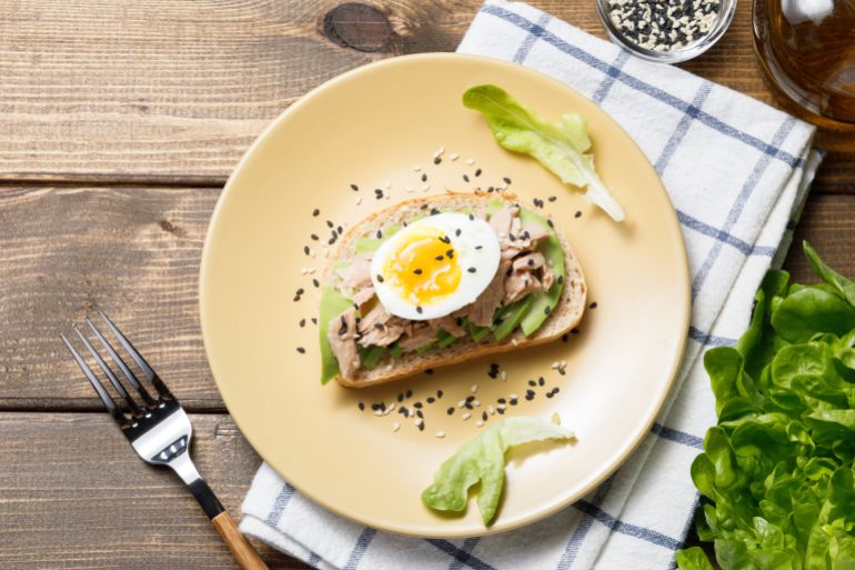 Avocado, canned tuna and boiled egg toast on wooden table background. Healthy food, avocado open sandwich for breakfast or lunch