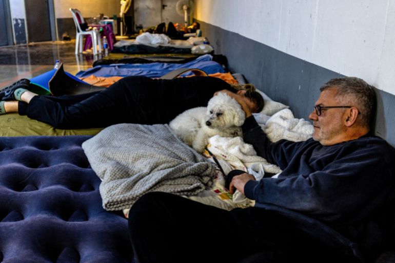 reuters_69a873d3-1772647379 A man comforts his dog as they shelter in an underground car park that functions as a bomb shelter, as sirens sound amid the U.S.-Israeli conflict with Iran, in Tel Aviv, Israel, March 4, 2026. REUTERS/Ronen Zvulun