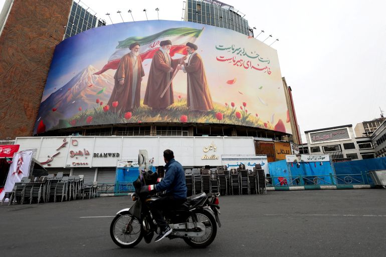 A man on a motorcycle looks at a large billboard featuring Iran's new Supreme Leader Mojtaba Khamenei, and late Supreme Leaders Ayatollah Ali Khamenei and Ayatollah Ruhollah Khomeini, amid the U.S.-Israeli conflict with Iran, in Tehran, Iran, March 12, 2026. REUTERS/Alaa Al-Marjani TPX IMAGES OF THE DAY
