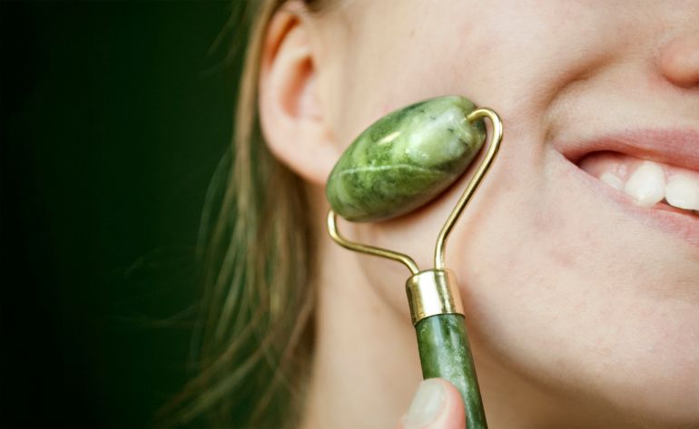Fragment of the face. A young, joyful woman uses a jade roller to massage her face. Real skin. Selective focus.