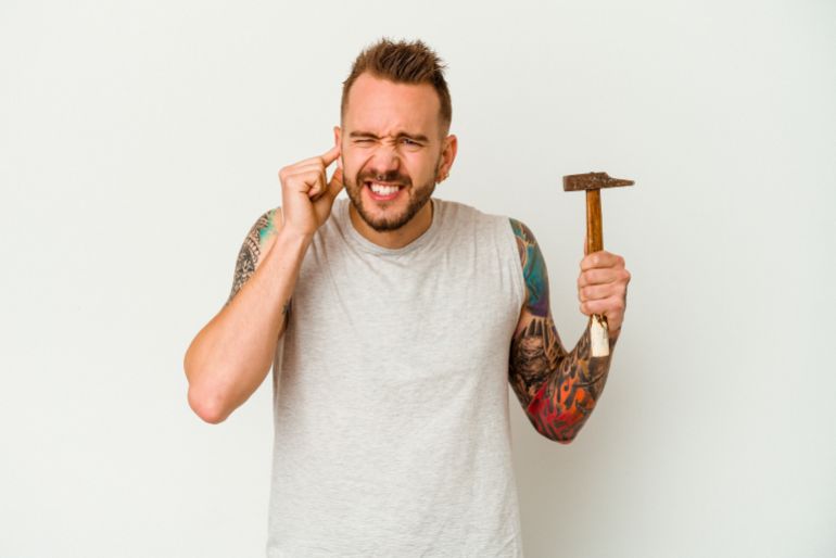 Young tattooed caucasian man isolated on white background covering ears with hands.